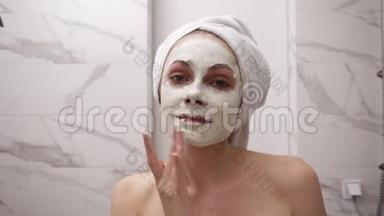 年轻漂亮的女人头上戴着白毛巾的肖像，正在涂<strong>上新</strong>鲜的白色厚<strong>面膜</strong>，并在脸上擦洗